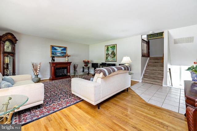 living area with visible vents, wood finished floors, stairway, baseboards, and a glass covered fireplace
