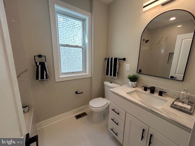 bathroom with vanity, visible vents, a shower, toilet, and baseboards