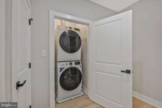 clothes washing area with baseboards, stacked washer and dryer, laundry area, and light wood-style flooring