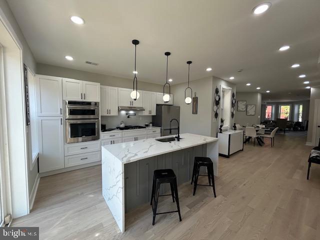 kitchen with light stone countertops, light wood finished floors, a breakfast bar area, stainless steel appliances, and white cabinetry