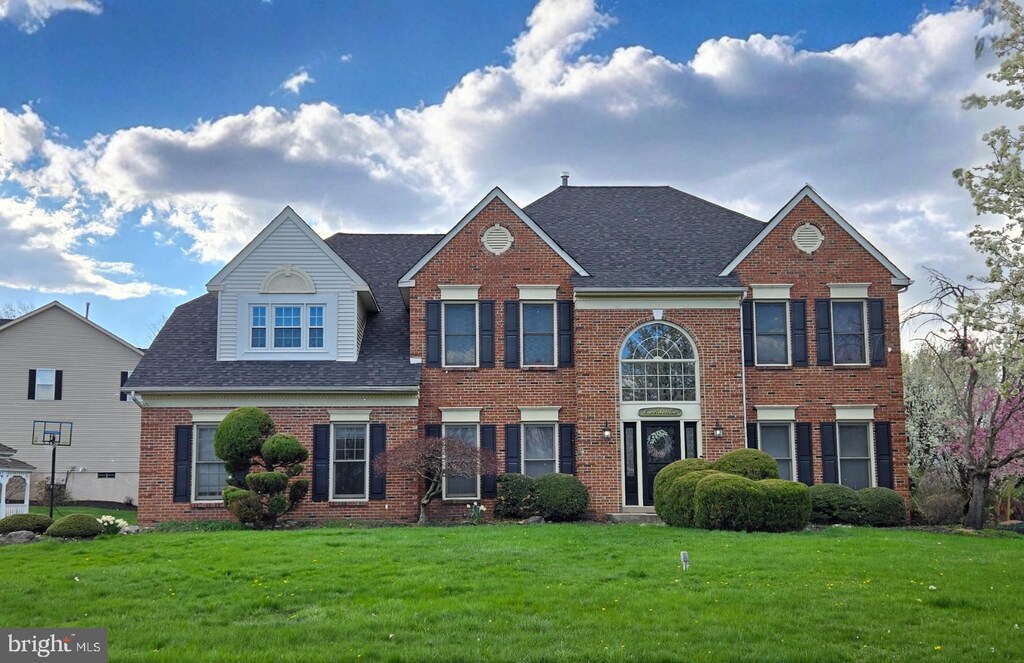 view of front facade featuring brick siding, a front yard, and roof with shingles