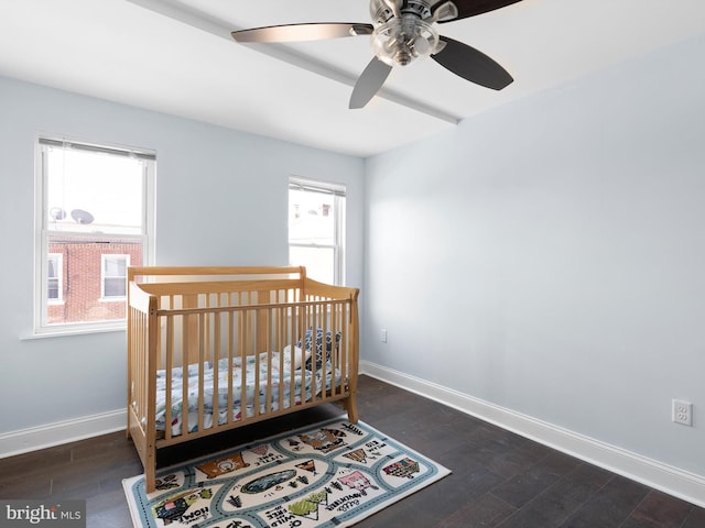 bedroom with baseboards, dark wood finished floors, ceiling fan, and a crib