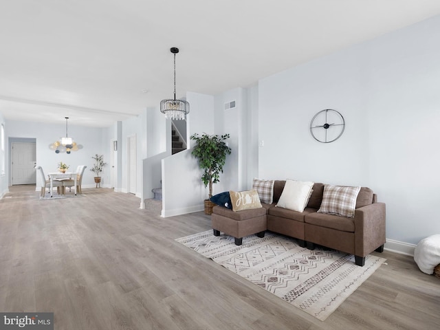living room featuring a notable chandelier, stairs, baseboards, wood finished floors, and visible vents