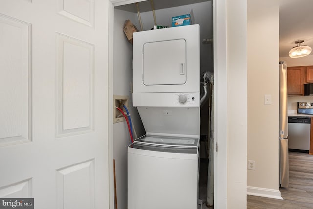 laundry room featuring baseboards, laundry area, stacked washer and dryer, and wood finished floors