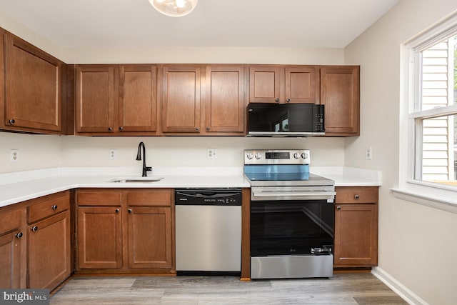 kitchen with light wood-type flooring, a sink, brown cabinets, and stainless steel appliances