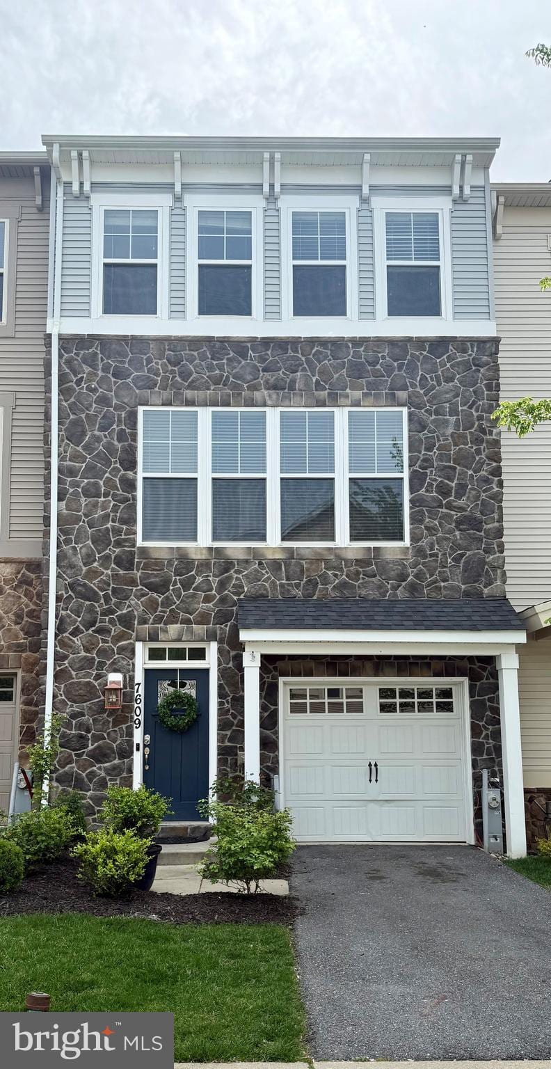 view of front of home with an attached garage, aphalt driveway, and stone siding
