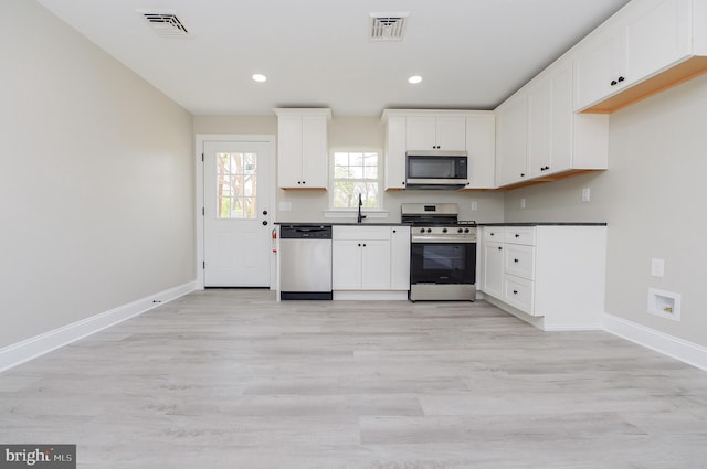 kitchen with dark countertops, appliances with stainless steel finishes, baseboards, light wood-type flooring, and visible vents