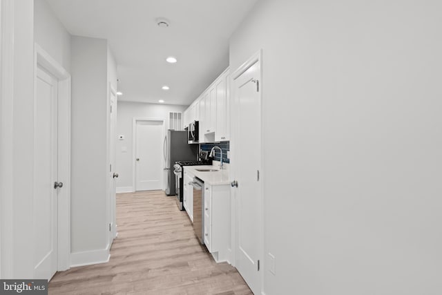 hallway featuring light wood-style floors, recessed lighting, baseboards, and a sink