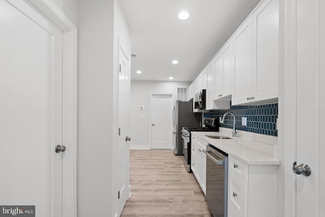 kitchen featuring tasteful backsplash, light wood-type flooring, a sink, stainless steel appliances, and white cabinetry