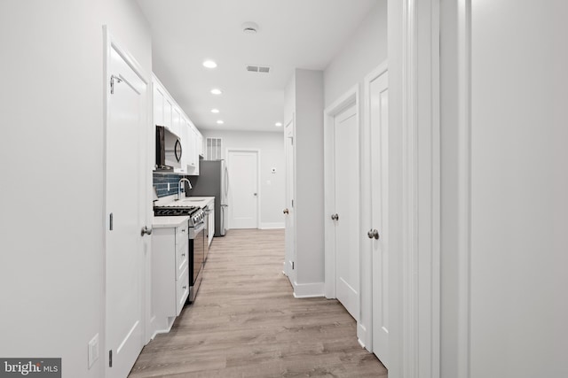 hall featuring visible vents, baseboards, recessed lighting, a sink, and light wood-style flooring