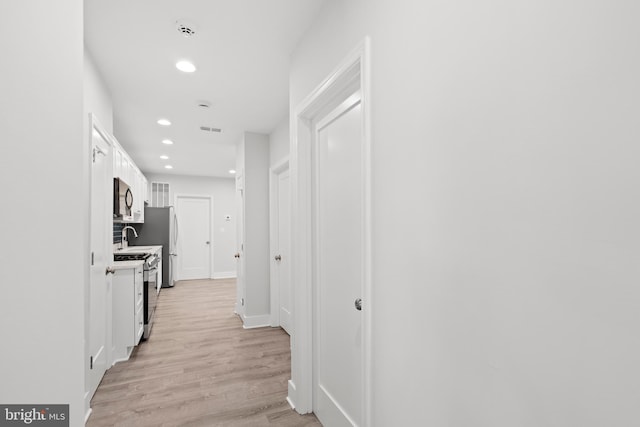 corridor with visible vents, light wood-style floors, baseboards, recessed lighting, and a sink