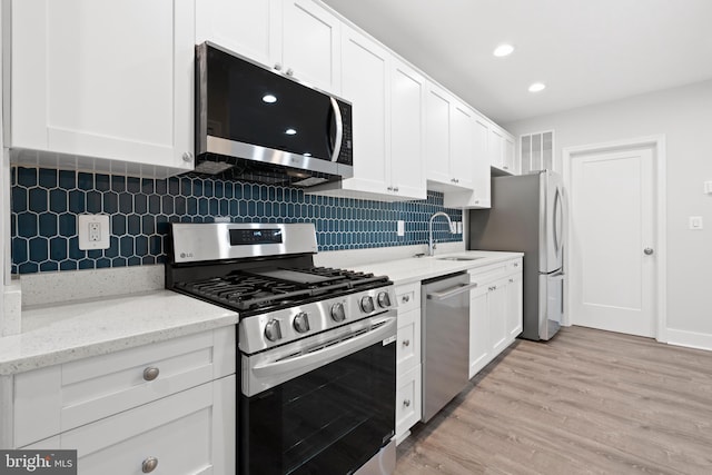 kitchen featuring white cabinets, tasteful backsplash, a sink, light wood-style flooring, and appliances with stainless steel finishes