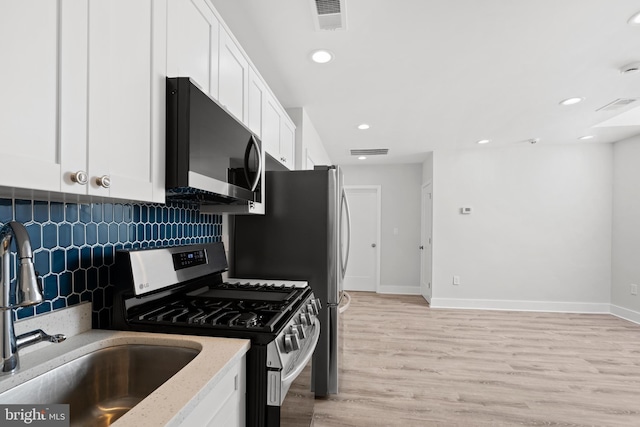 kitchen featuring visible vents, white cabinets, tasteful backsplash, a sink, and gas stove