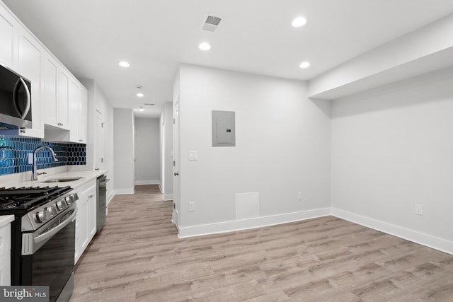 kitchen with light countertops, white cabinets, electric panel, a sink, and stainless steel appliances