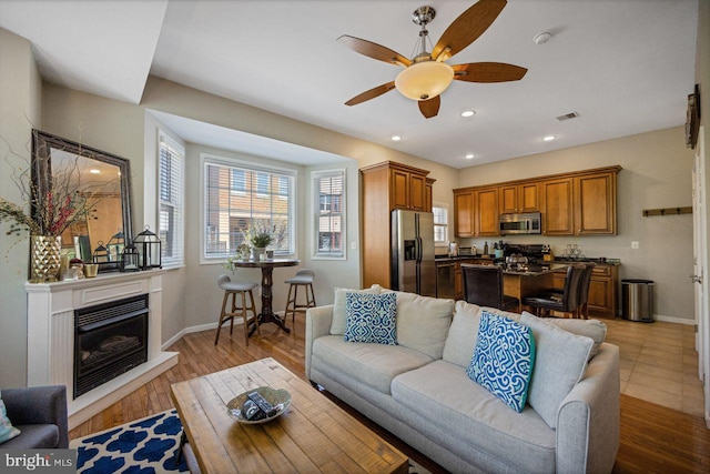 living room with visible vents, baseboards, ceiling fan, and a glass covered fireplace