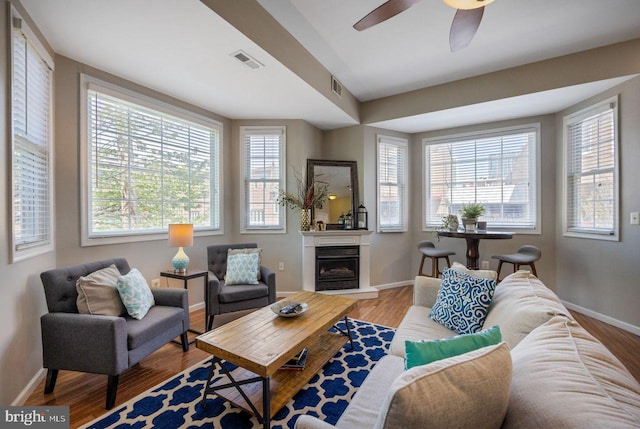 living room featuring visible vents, a ceiling fan, baseboards, and wood finished floors