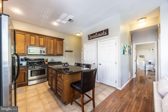 kitchen featuring brown cabinetry, a breakfast bar area, a center island, dark stone counters, and stainless steel appliances