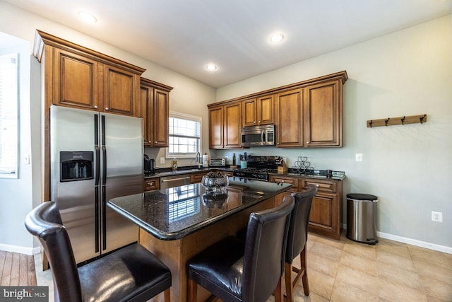 kitchen featuring baseboards, a kitchen bar, brown cabinets, a sink, and stainless steel appliances