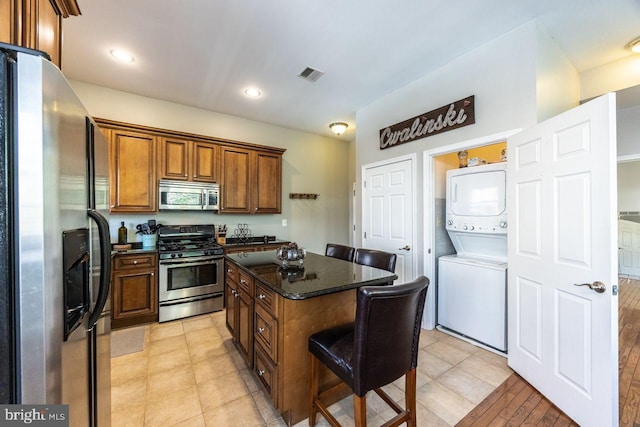 kitchen with brown cabinets, stacked washer / drying machine, appliances with stainless steel finishes, a center island, and visible vents