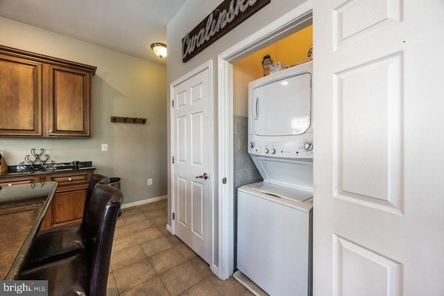 laundry area featuring baseboards, tile patterned flooring, stacked washer / drying machine, and laundry area