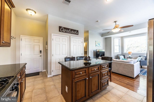 kitchen with visible vents, a ceiling fan, dark stone countertops, light tile patterned floors, and gas stove