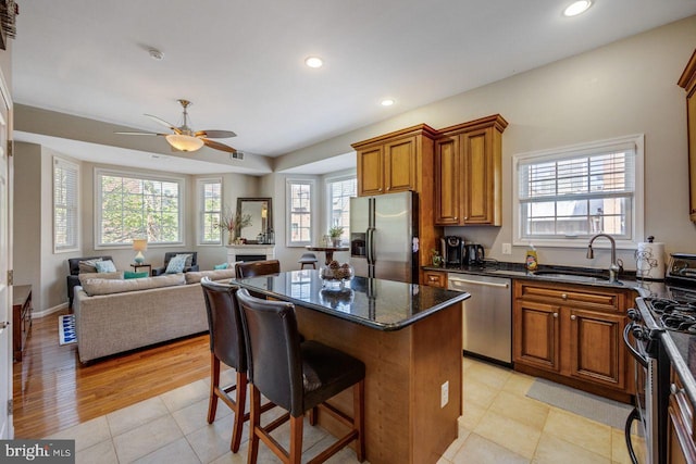 kitchen with brown cabinets, appliances with stainless steel finishes, a sink, a ceiling fan, and a kitchen island