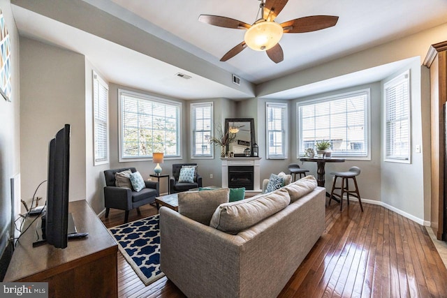 living room with a ceiling fan, visible vents, a fireplace, baseboards, and dark wood-type flooring