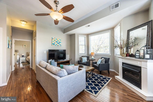 living area featuring baseboards, ceiling fan, wood-type flooring, and visible vents