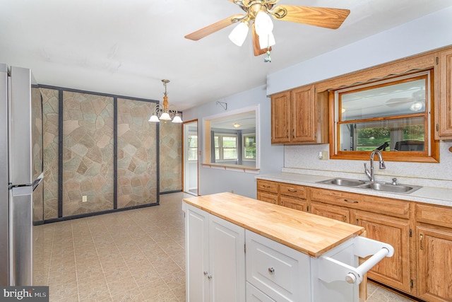 kitchen with a sink, wooden counters, ceiling fan with notable chandelier, freestanding refrigerator, and pendant lighting