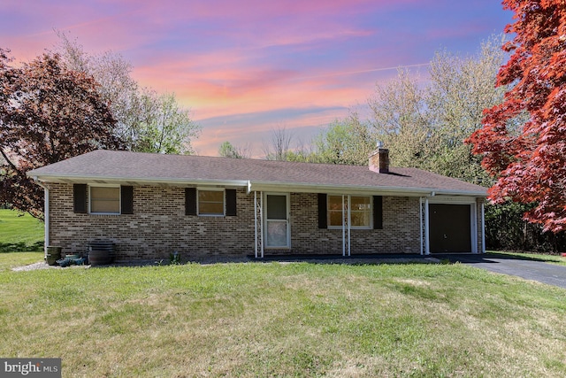 view of front facade featuring a garage, a front yard, a chimney, brick siding, and driveway