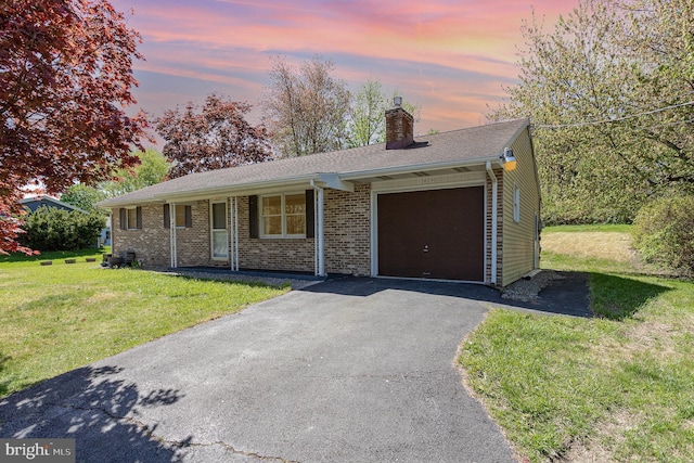 ranch-style home with an attached garage, brick siding, a chimney, a yard, and driveway