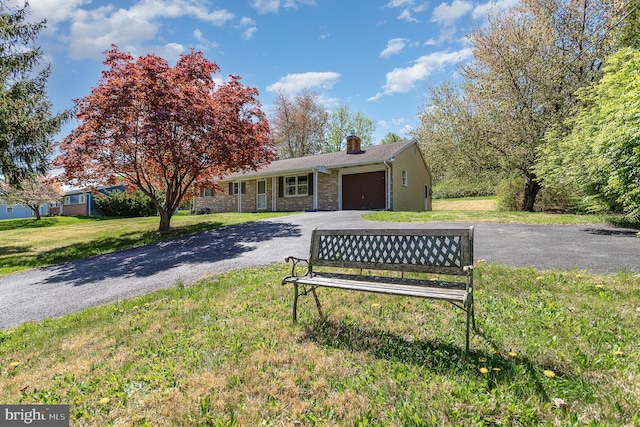 view of front of house with a garage, a chimney, a front yard, and aphalt driveway