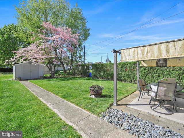 view of yard featuring a storage shed, an outbuilding, a fenced backyard, an outdoor fire pit, and a patio