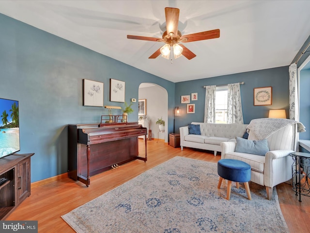 living area featuring arched walkways, ceiling fan, baseboards, and wood finished floors