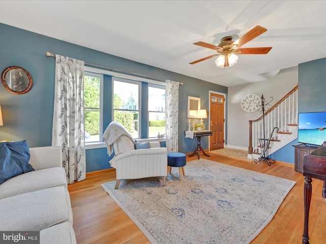 living room with baseboards, ceiling fan, stairway, and light wood-style floors