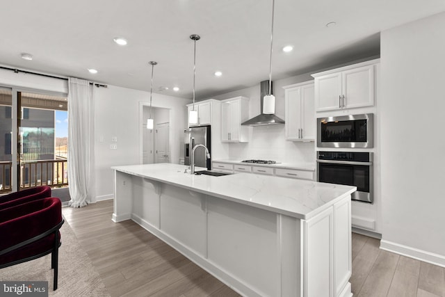 kitchen with light wood finished floors, wall chimney exhaust hood, stainless steel appliances, baseboards, and a large island