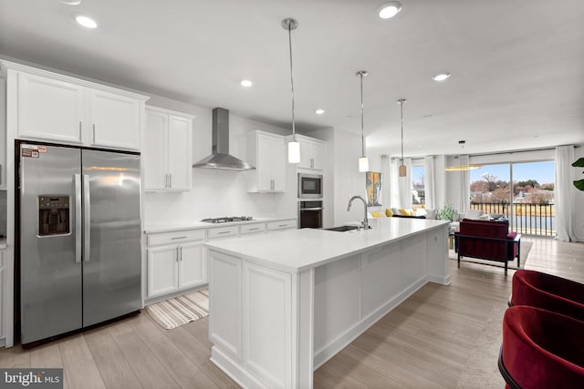 kitchen featuring wall chimney range hood, a sink, light countertops, stainless steel appliances, and light wood-type flooring