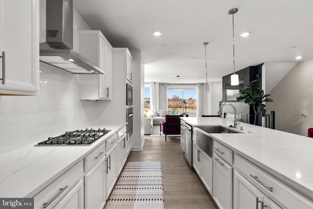 kitchen featuring appliances with stainless steel finishes, tasteful backsplash, a sink, white cabinets, and wall chimney exhaust hood