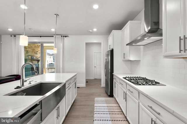 kitchen with decorative backsplash, wall chimney exhaust hood, white cabinets, a sink, and appliances with stainless steel finishes