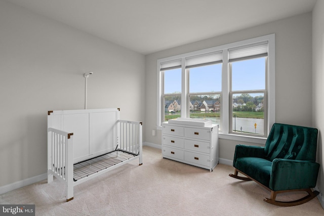 bedroom with baseboards, a crib, and light colored carpet