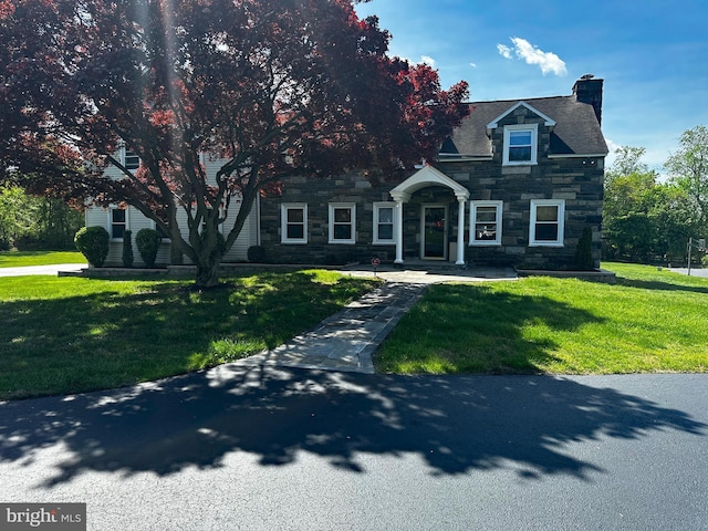 view of front of home featuring a chimney, stone siding, and a front lawn