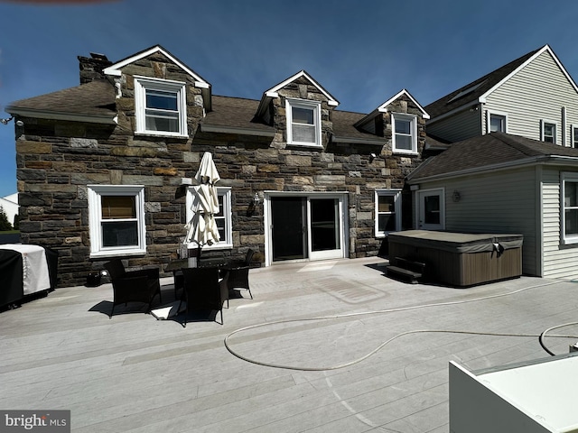 rear view of house with a hot tub, a patio, a chimney, and stone siding