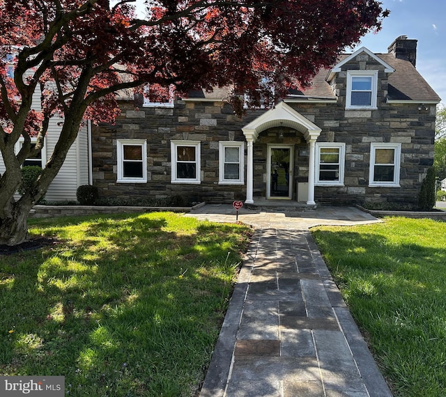 view of front facade featuring a chimney, a front yard, and stone siding