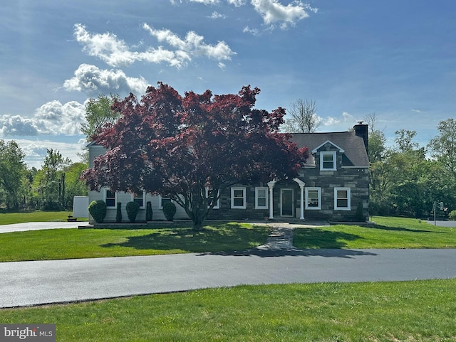 view of front of house featuring a chimney, stone siding, and a front yard