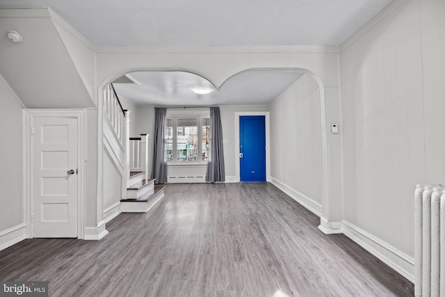 entrance foyer featuring arched walkways, radiator, wood finished floors, and stairway