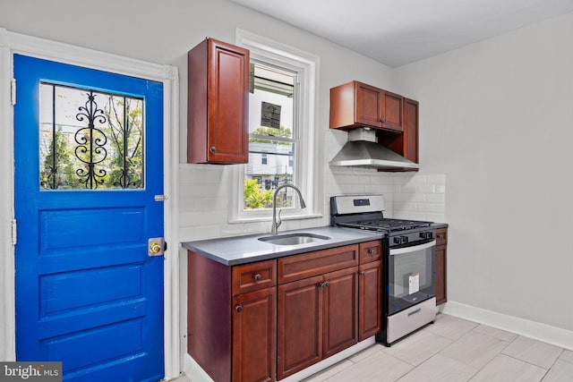 kitchen featuring decorative backsplash, stainless steel gas stove, a healthy amount of sunlight, wall chimney exhaust hood, and a sink