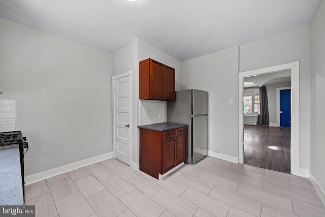 kitchen with baseboards, freestanding refrigerator, arched walkways, and dark countertops