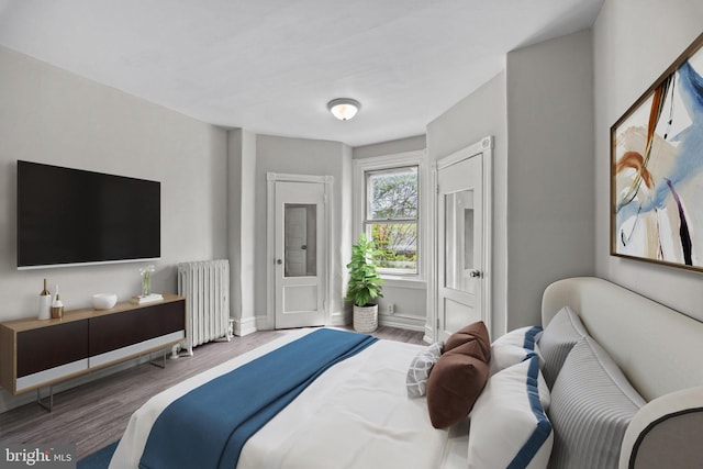 bedroom featuring radiator heating unit, baseboards, and wood finished floors