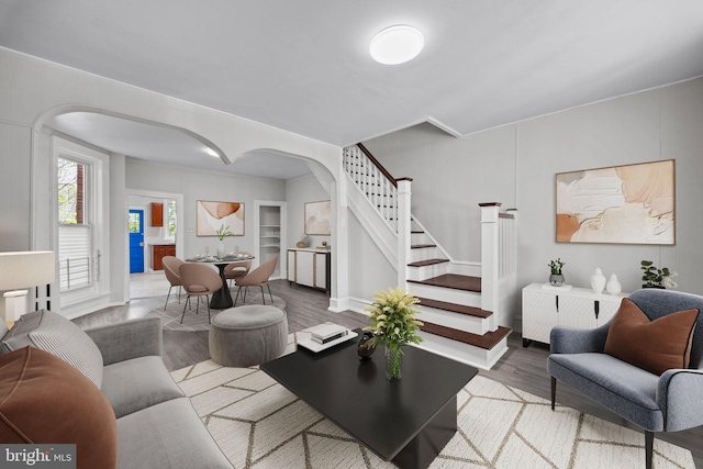 living area featuring built in features, arched walkways, stairs, and wood finished floors