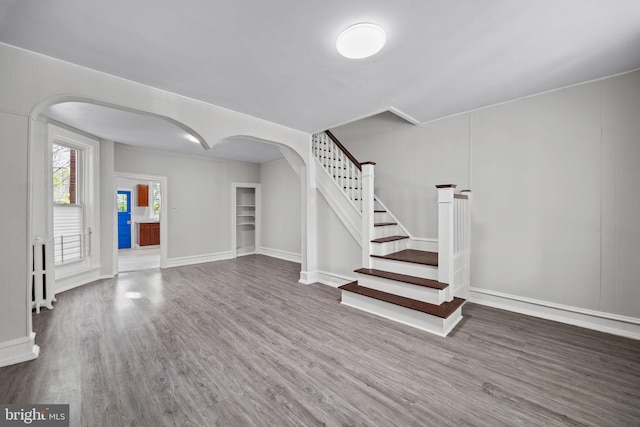interior space with arched walkways, baseboards, wood finished floors, and stairway